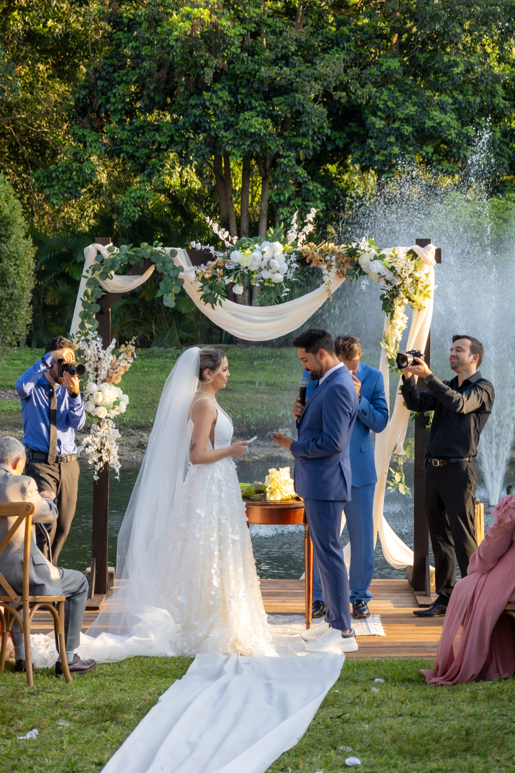 Bride and groom exchanging vows by floral arch and fountain at Saint Patrick Palace outdoor ceremony.