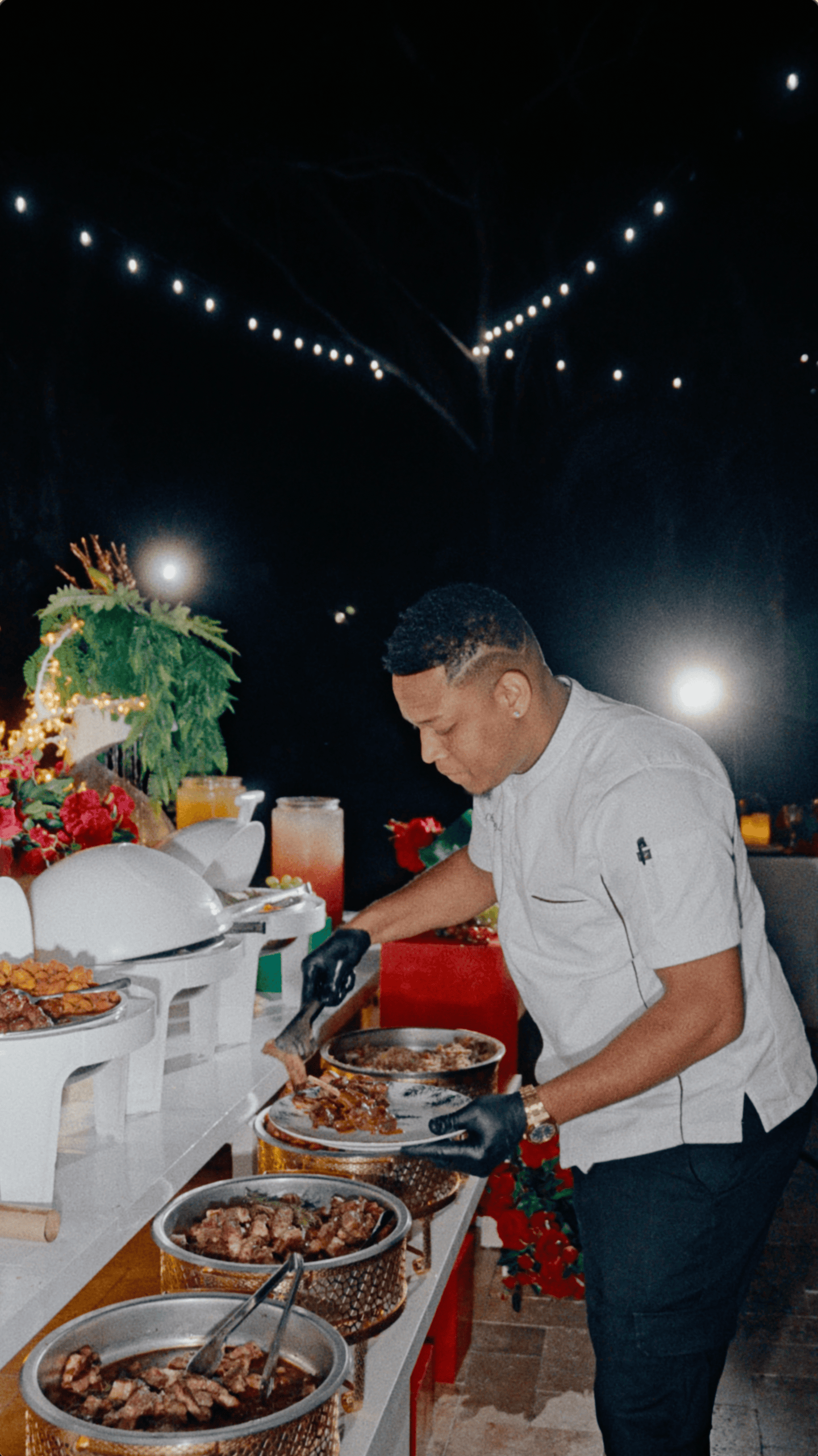 Catering professional plates a meal at an outdoor holiday buffet with chafing dishes and festive floral décor.