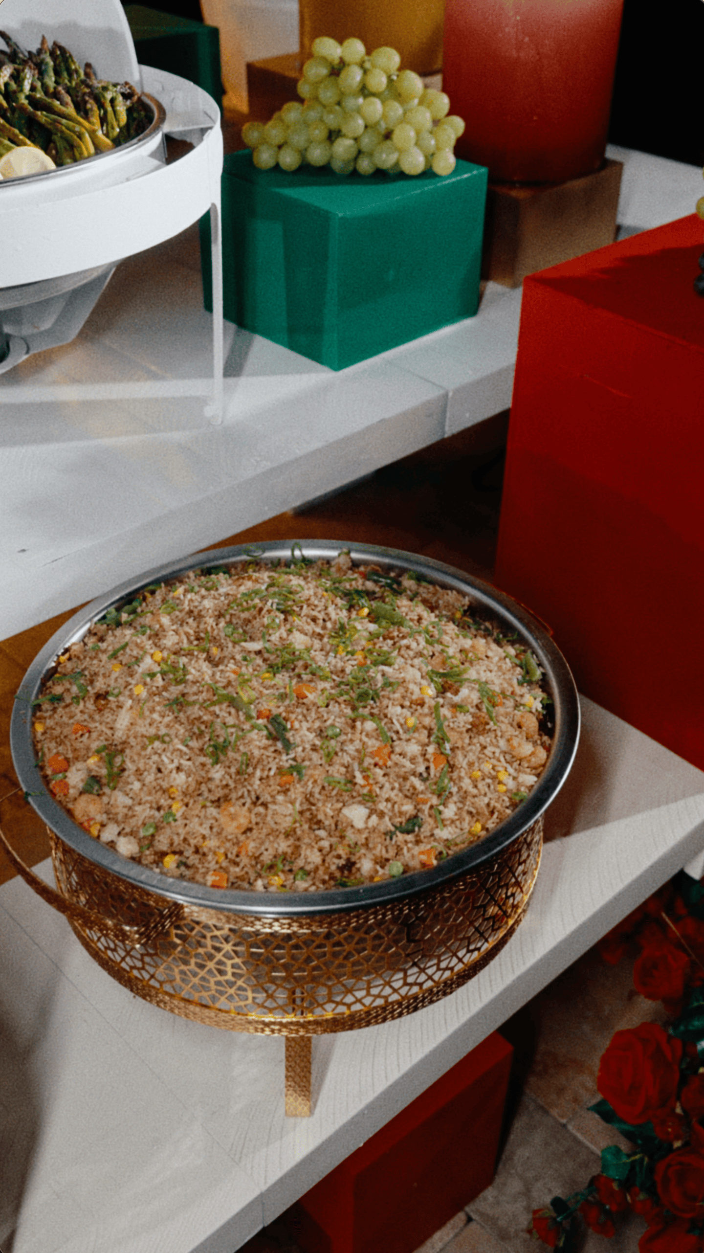 Large bowl of seasoned rice and vegetables displayed in an elegant gold stand at a holiday catering buffet.