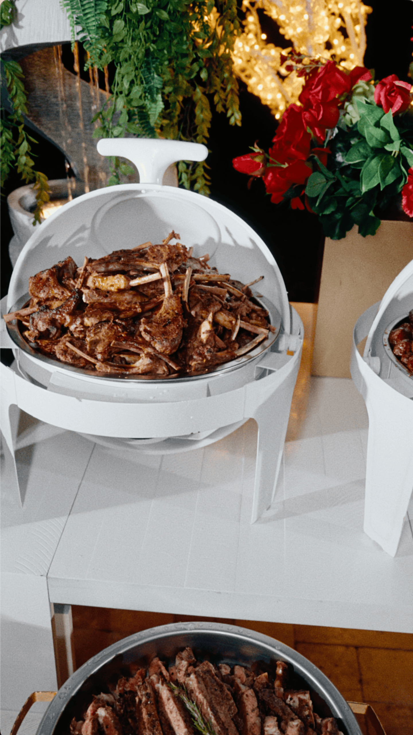 Roasted meat displayed in a white chafing dish surrounded by festive red flowers and holiday decorations.