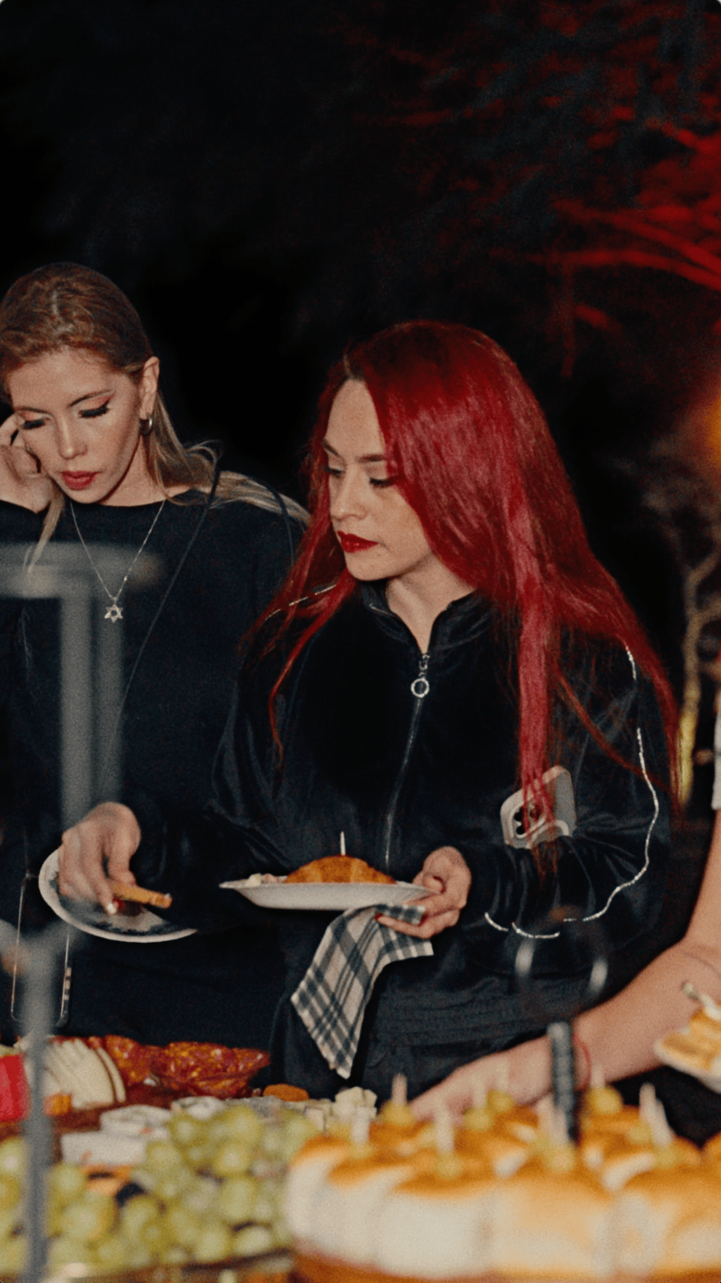 Two guests selecting food from a catered holiday buffet during an outdoor evening celebration.