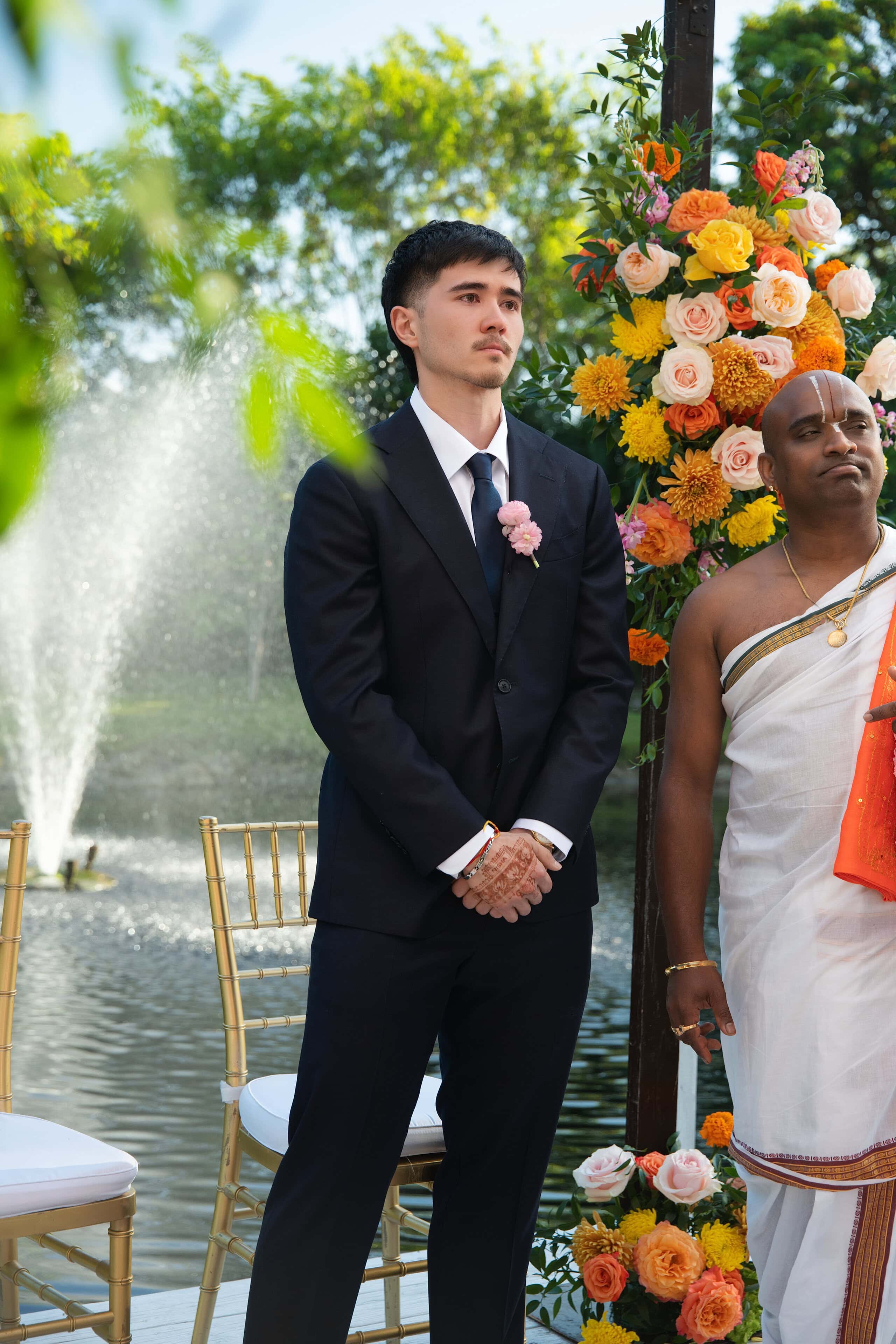 Groom standing beneath a floral mandap beside the lake during an Indian wedding ceremony at Saint Patrick Palace.