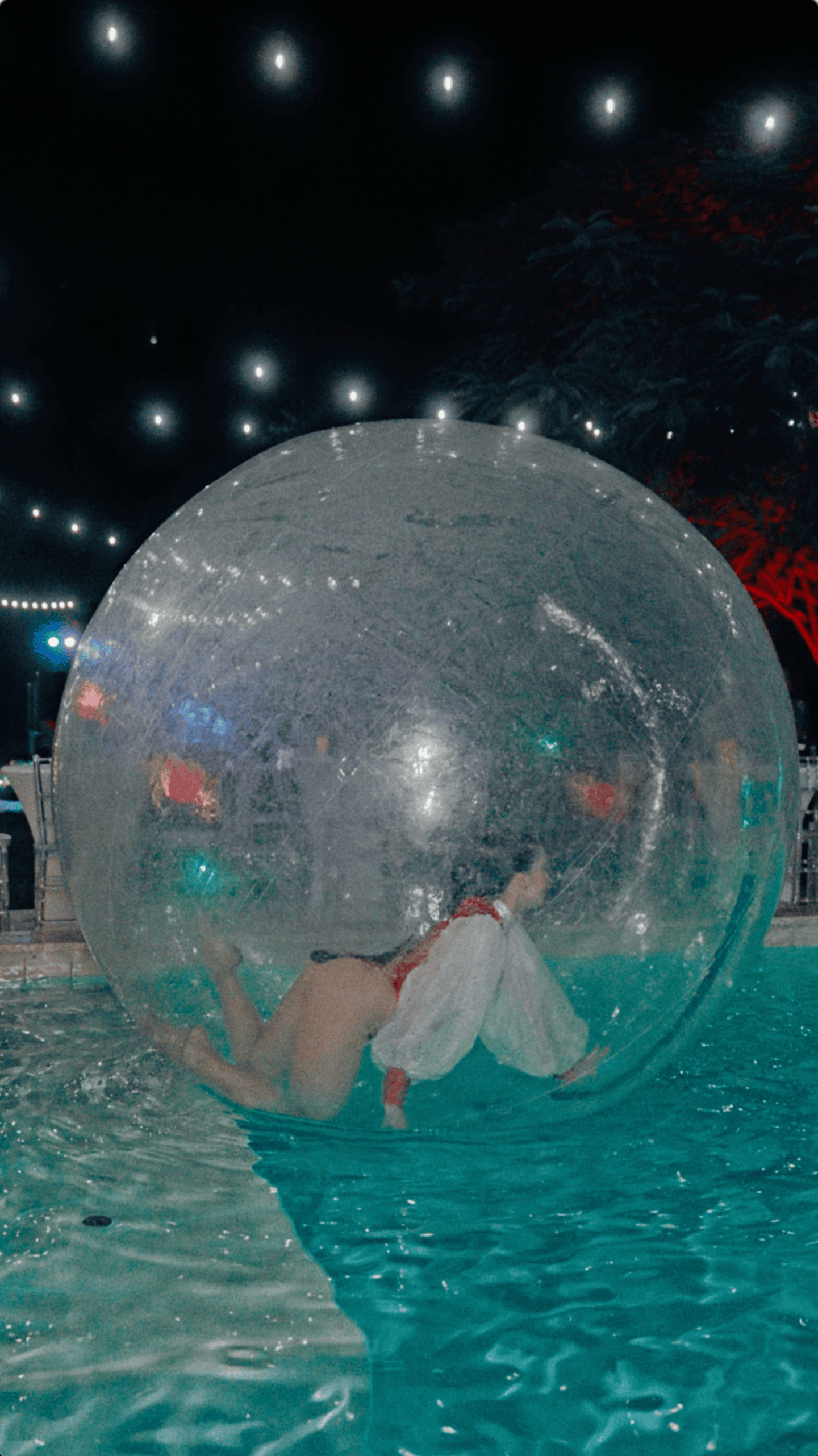 Performer in a red and white costume moving inside a transparent inflatable ball on a swimming pool.
