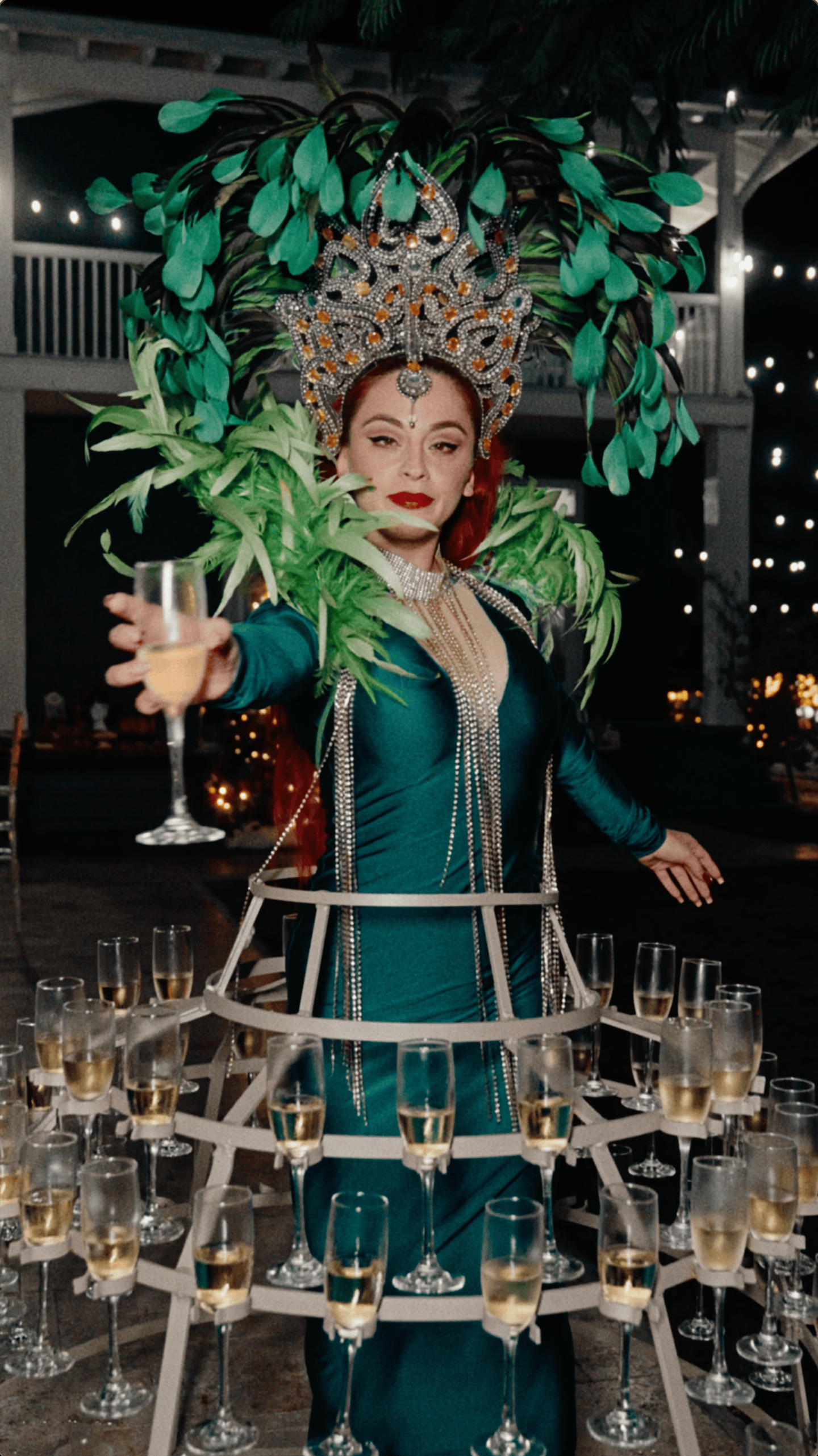 Emerald-green champagne skirt performer offering a champagne flute during an outdoor Christmas party.