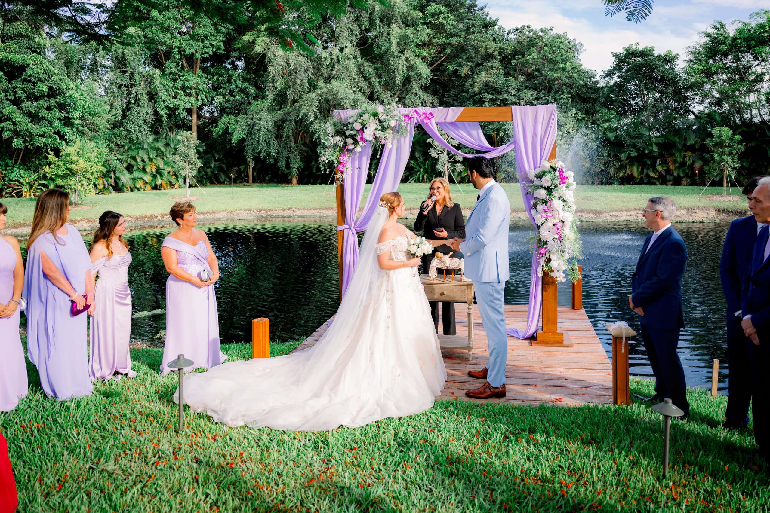 Interfaith wedding ceremony with officiant under floral arch at waterfront estate in South Florida