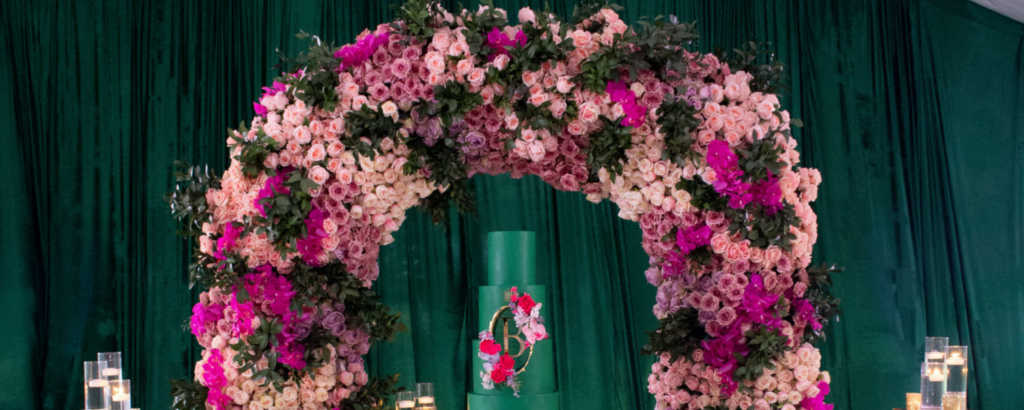 Massive lush floral arch with pink and purple roses framing an emerald green wedding cake