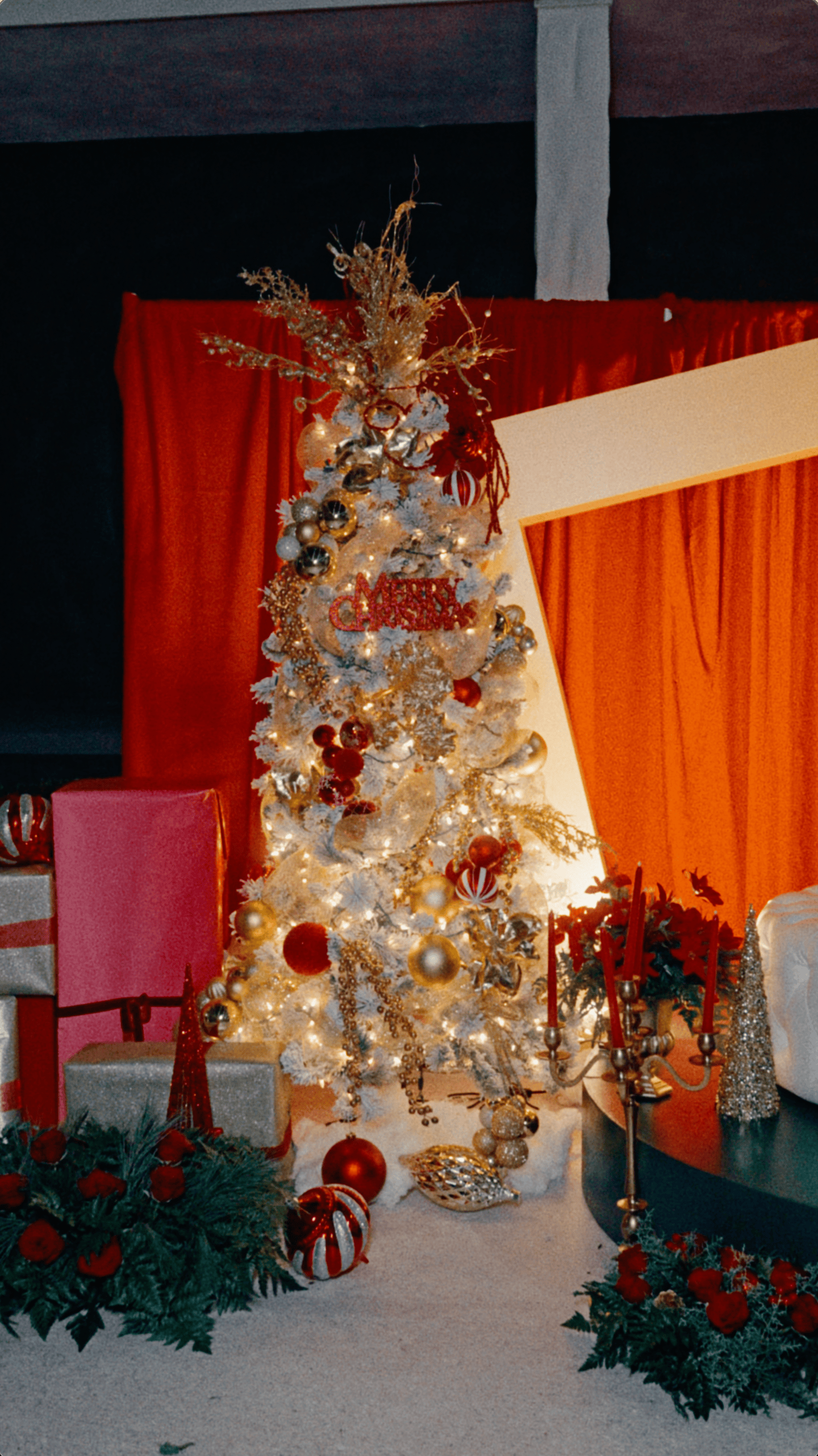 Luxury Christmas display with a decorated white tree, oversized gifts, red drapery, and festive floral arrangements.