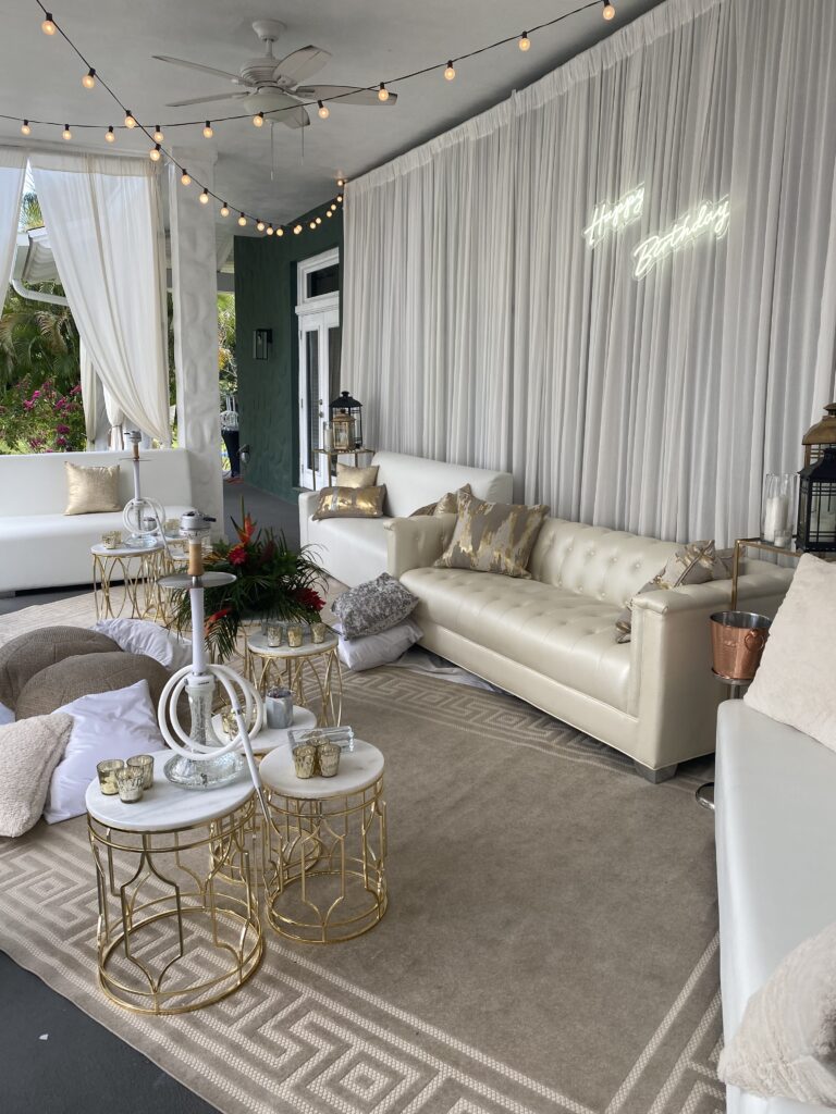 Luxury outdoor lounge with white sofas and gold décor for a tropical 60th birthday garden brunch.