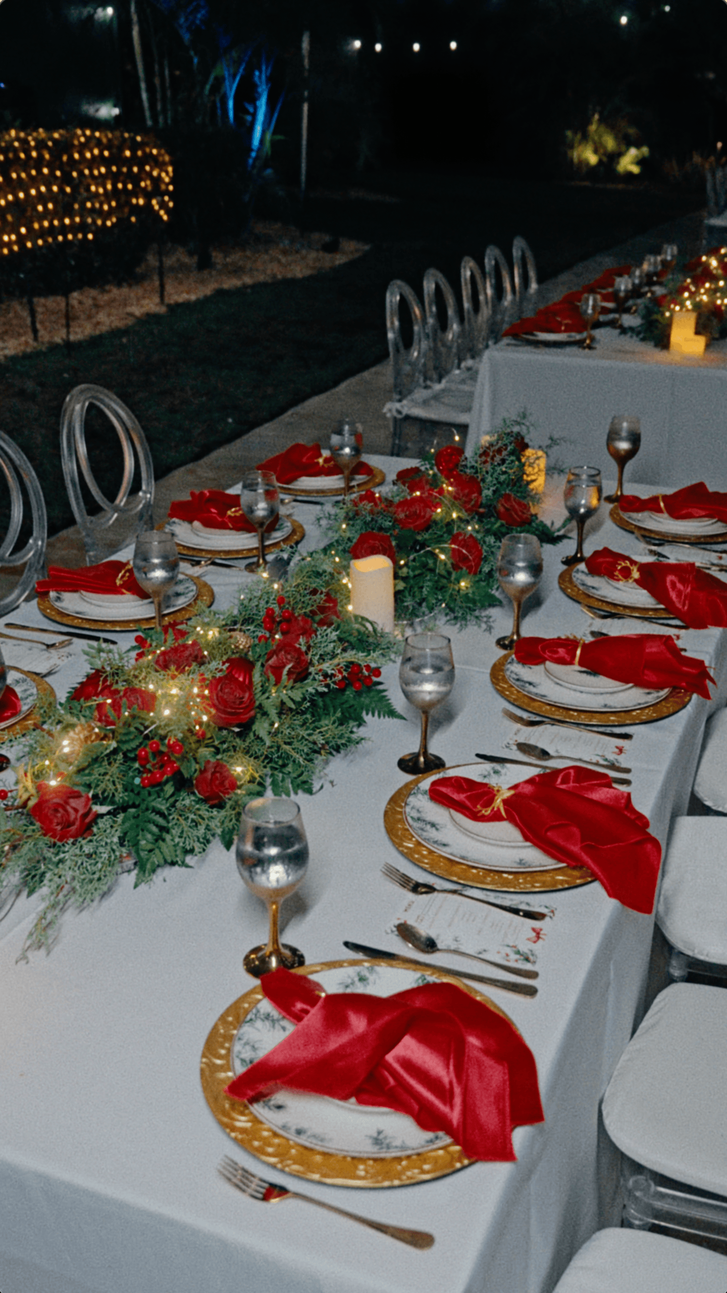 Outdoor Christmas dinner tables with red napkins, gold chargers, floral centerpieces, and elegant seating.