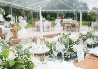 Close up detail shot of wedding table setting with white roses, eucalyptus greenery, gold candlesticks, and wooden tables.