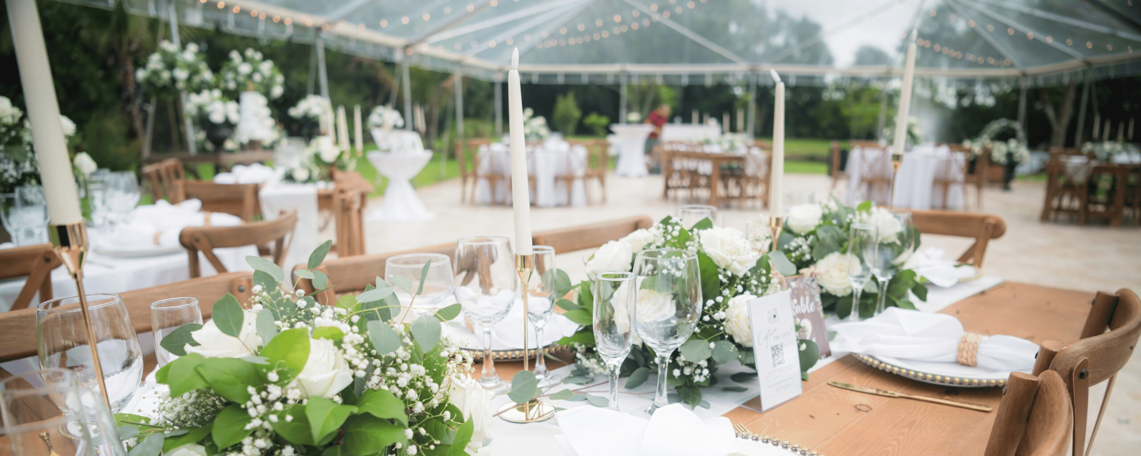 Close up detail shot of wedding table setting with white roses, eucalyptus greenery, gold candlesticks, and wooden tables.