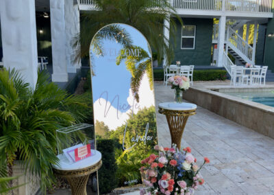Mirror welcome sign with floral arrangement by pool at South Florida quince venue.