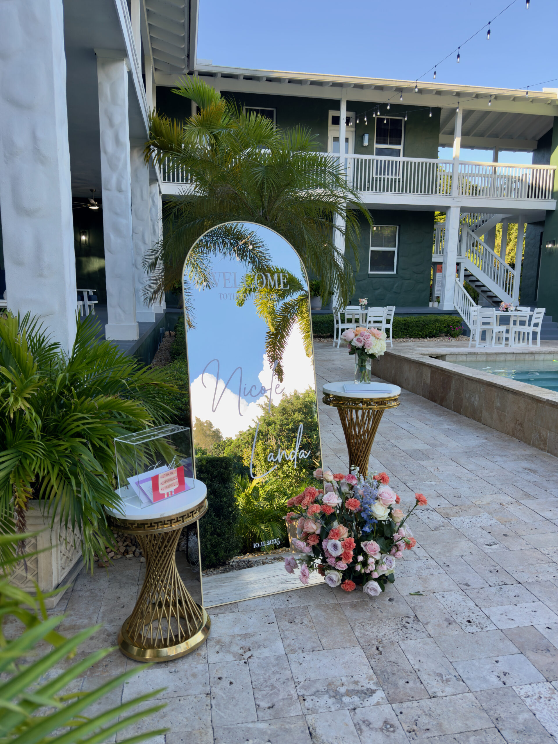 Mirror welcome sign with floral arrangement by pool at South Florida quince venue.