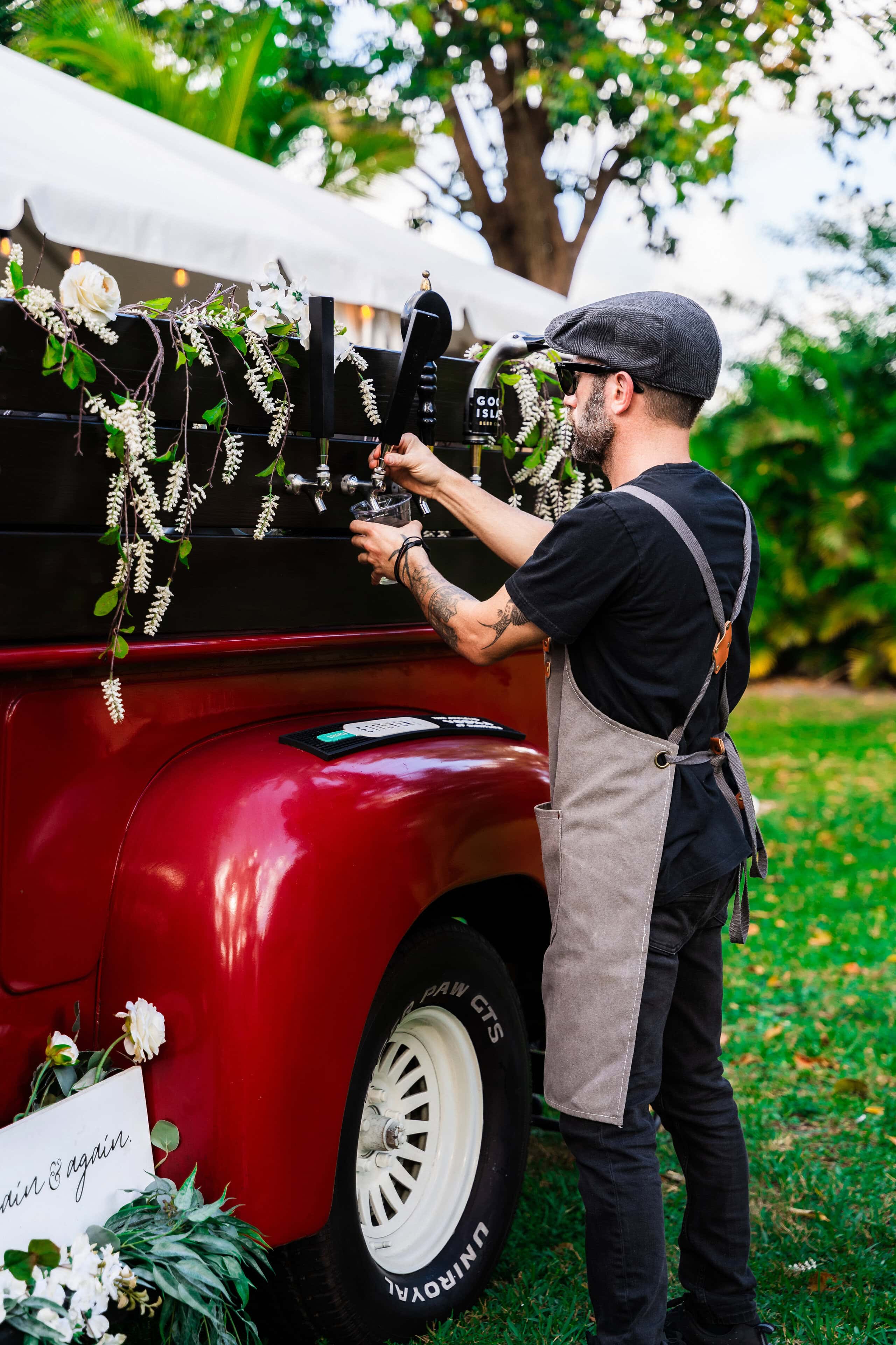 Professional bartender serving draft beer from a vintage mobile wedding bar during an outdoor wedding reception.