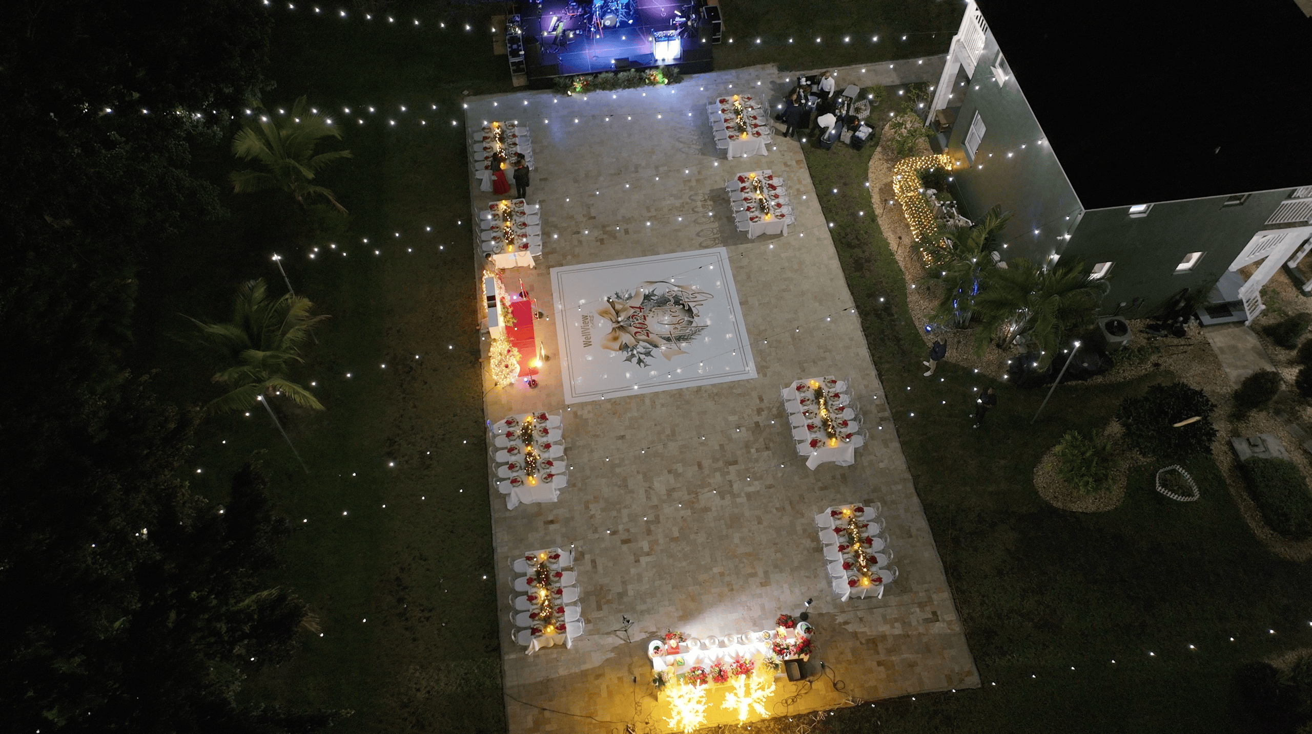 Elevated view of an outdoor holiday party with decorated banquet tables, a custom dance floor, and stage.