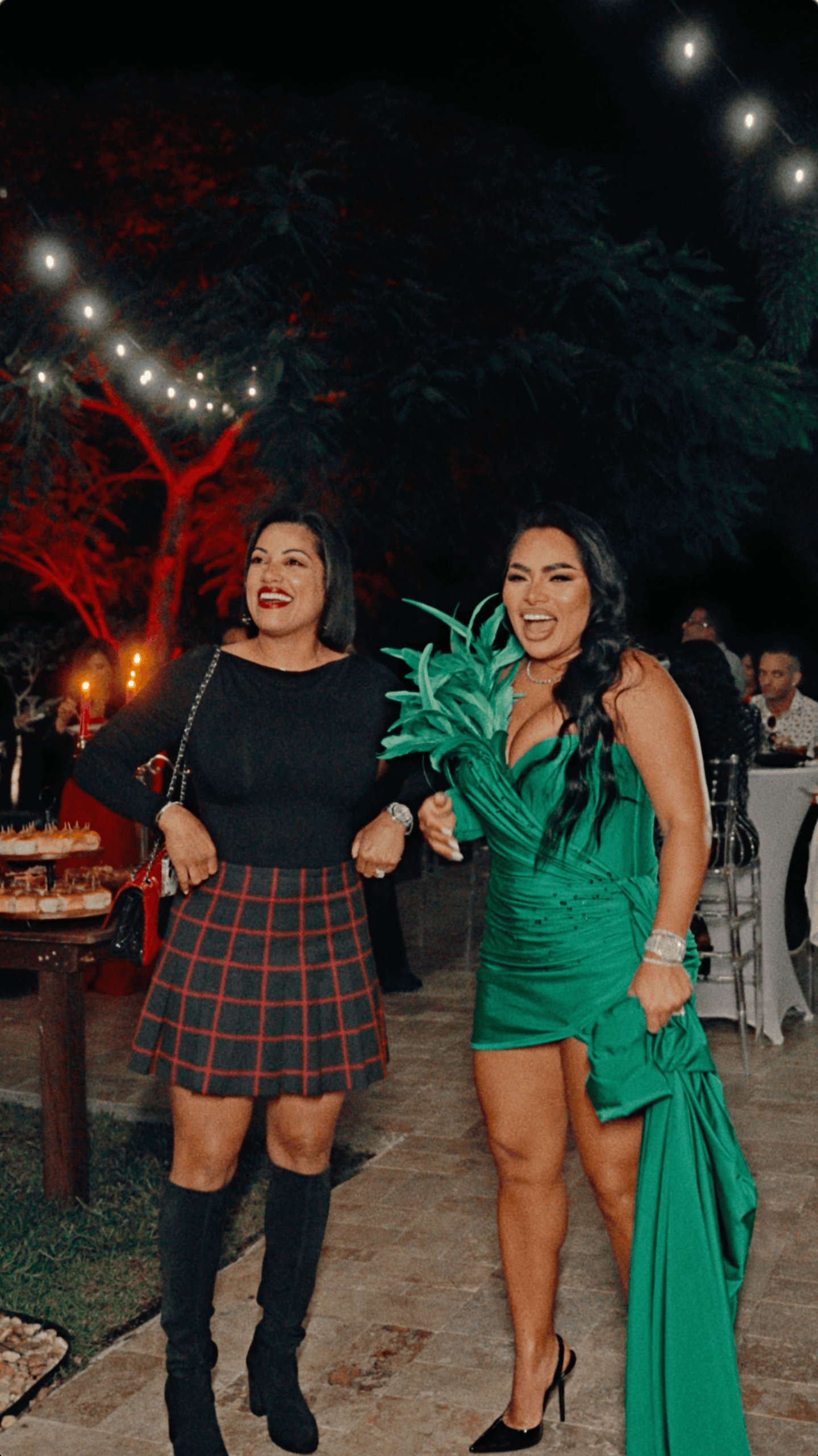 Two smiling holiday party guests walking together beneath bistro lights at an outdoor estate celebration.