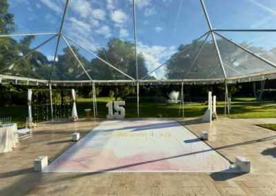 Outdoor quinceañera reception with clear tent, custom dance floor, and marquee 15 at Saint Patrick Palace.