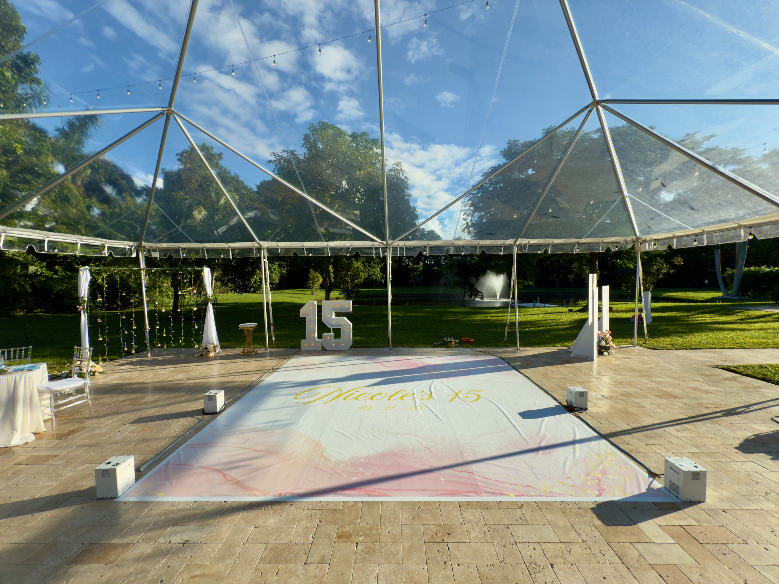 Outdoor quinceañera reception with clear tent, custom dance floor, and marquee 15 at Saint Patrick Palace.