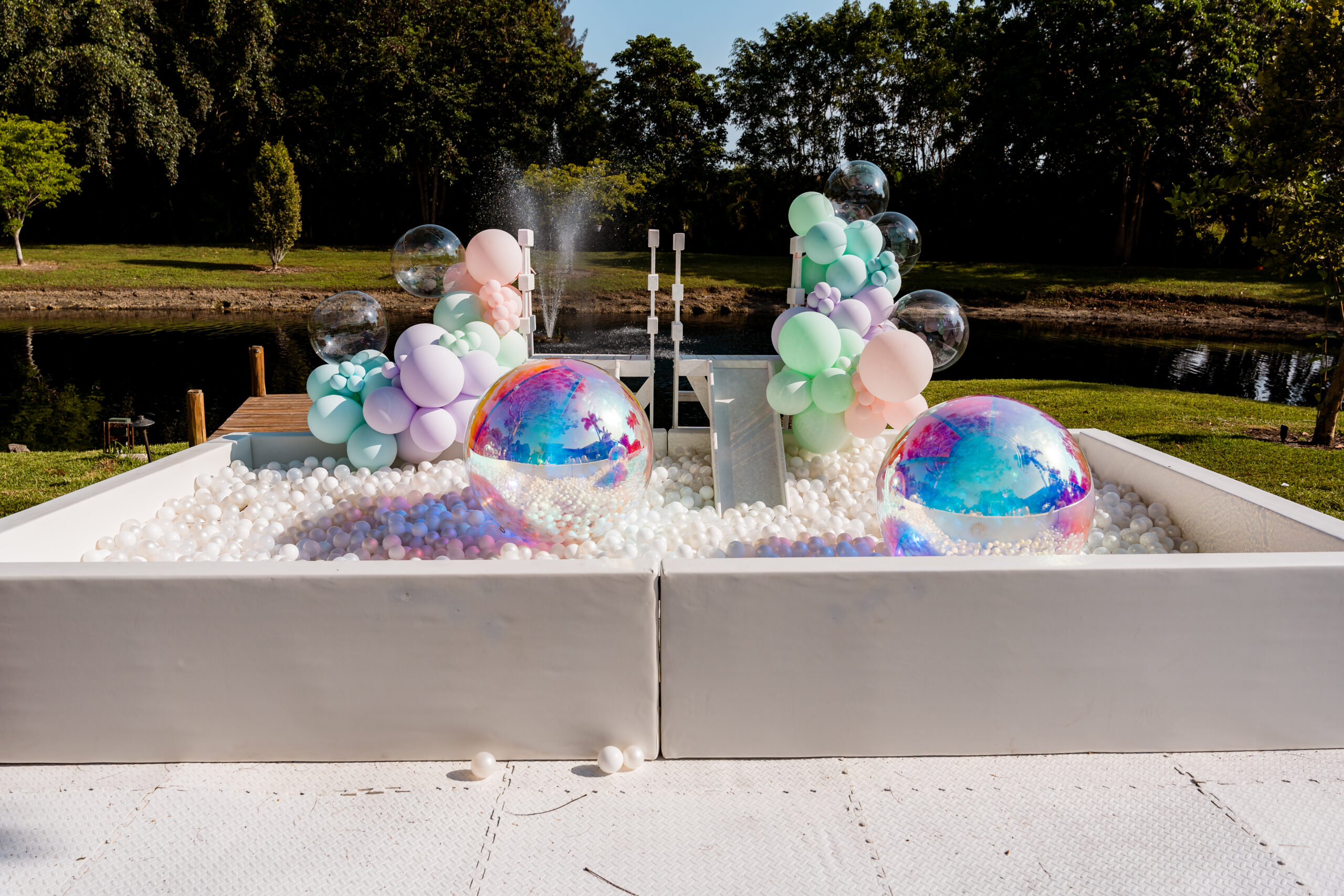 Pastel soft play zone with slide, balloons, and iridescent beach balls for 1st birthday by the water
