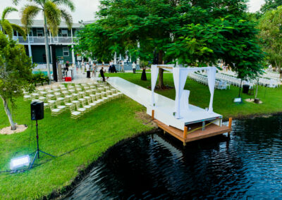 Outdoor lakefront wedding ceremony with white aisle, ghost chairs, and draped arch at Saint Patrick Palace.
