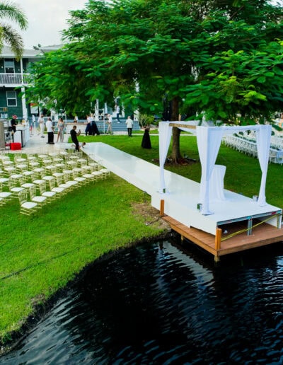 Outdoor lakefront wedding ceremony with white aisle, ghost chairs, and draped arch at Saint Patrick Palace.