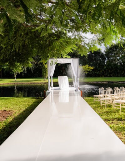 Elegant outdoor wedding chuppah setup for ceremony with white aisle and lakeside altar at a luxury estate.