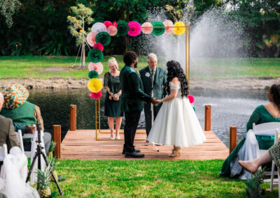 Couple exchanging vows at colorful outdoor lakeside wedding ceremony in South Florida.