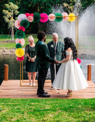 Couple exchanging vows at colorful outdoor lakeside wedding ceremony in South Florida.