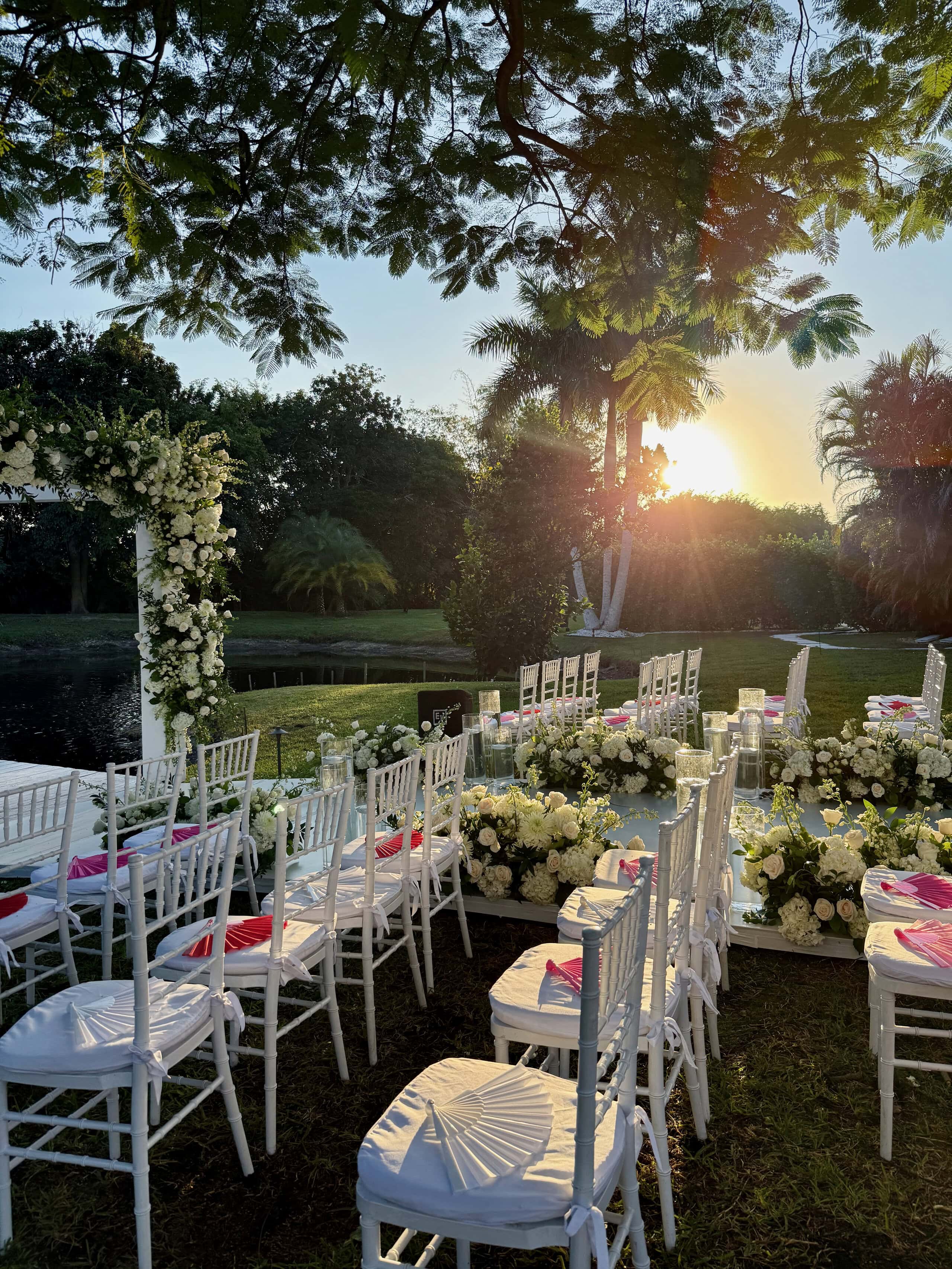 Outdoor sunset wedding ceremony with white chairs and floral arch at Saint Patrick Palace private estate in South Florida