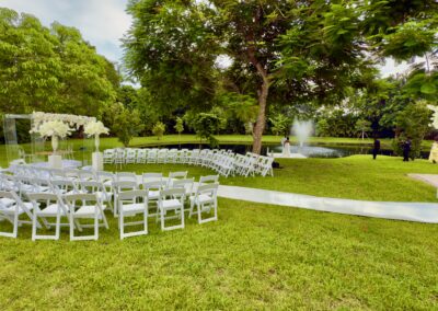 Outdoor wedding ceremony with white chairs, floral arch, and lakeside backdrop.