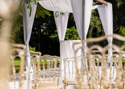 White draped wedding arch with gold chairs at an elegant outdoor ceremony by the water.