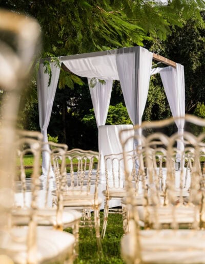 White chuppah draped with gold chairs at an elegant outdoor ceremony by the water.