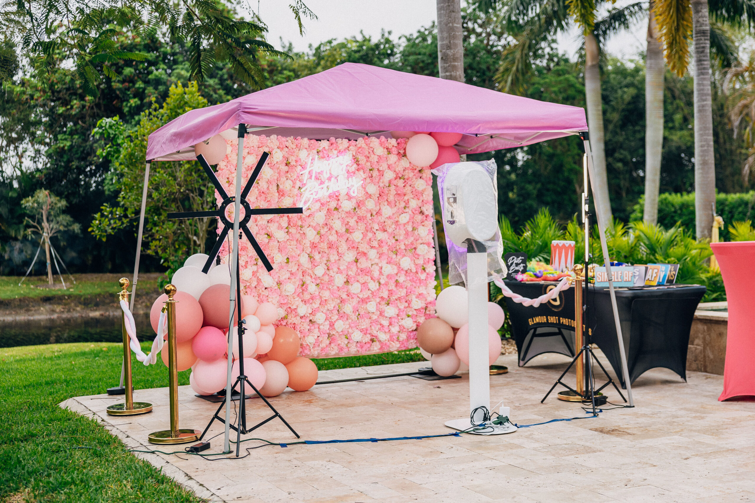 Pink glam photo booth with flower wall and props for fun party pictures.