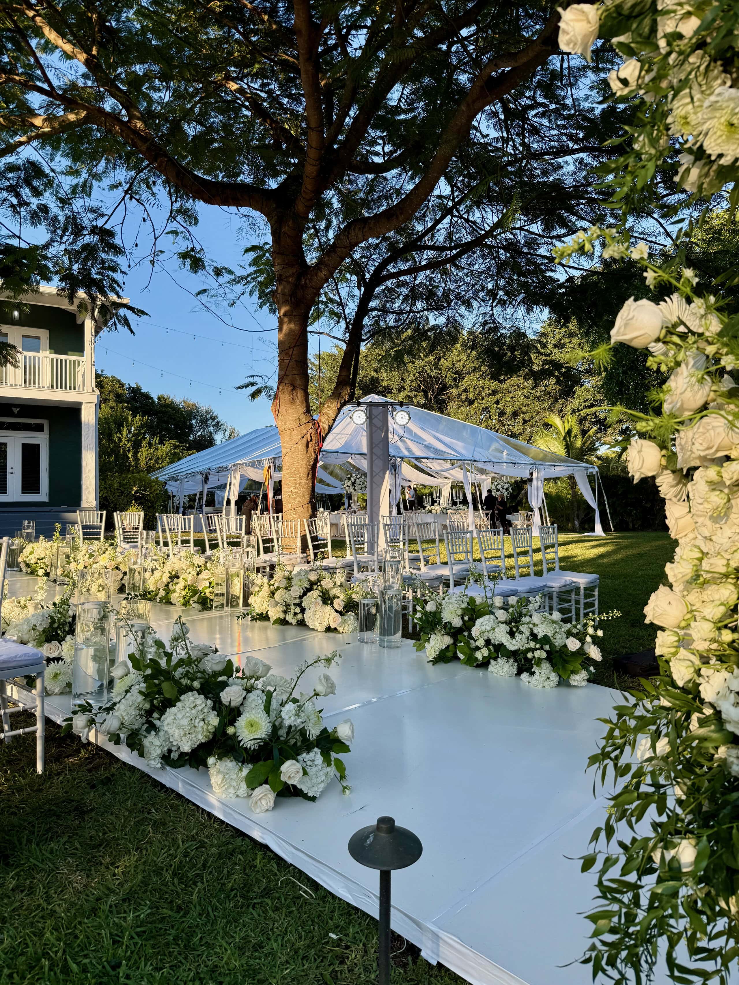 Private home wedding in South Florida with a floral outdoor ceremony and clear-top reception tent nearby.