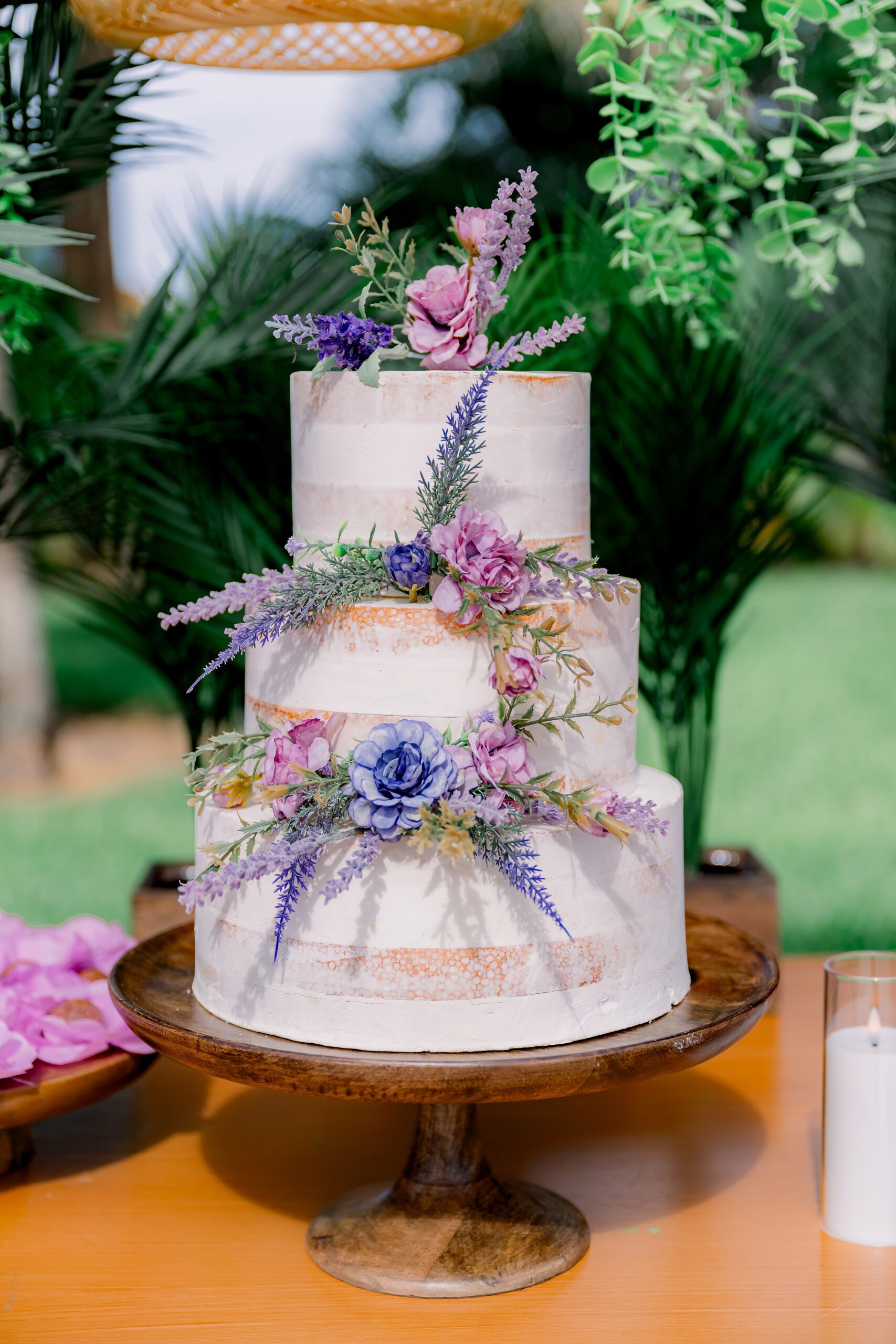 Three-tier wedding cake with lavender, blush, and blue florals at an outdoor summer wedding at Saint Patrick Palace.