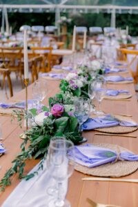 Wooden banquet table with greenery garland, lavender napkins, and gold accents at a summer wedding.