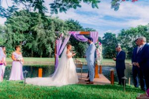 Bride and groom exchanging vows on the dock under a lavender-draped arch at a summer wedding at Saint Patrick Palace.
