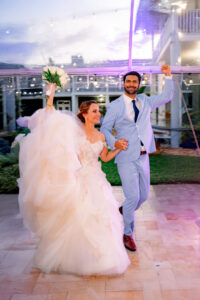 Bride and groom celebrating with a joyful grand entrance under a clear-top tent at a summer wedding.