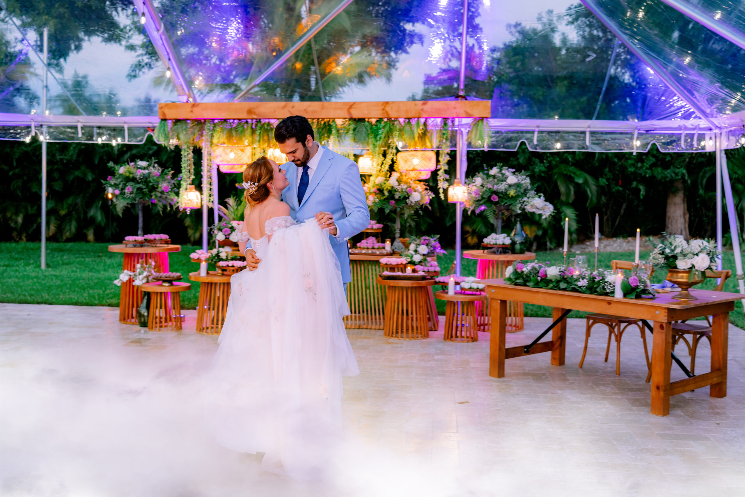 Couple sharing their first dance under a clear tent with lavender décor, florals, and glowing lights at Saint Patrick Palace.