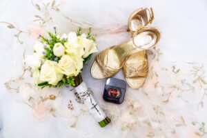 Summer wedding flat-lay with a gold heel, purple blooms, a bouquet, and styling elements at Saint Patrick Palace.