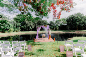 Romantic lakeside wedding ceremony with lavender draping and floral arch at Saint Patrick Palace, Davie FL.