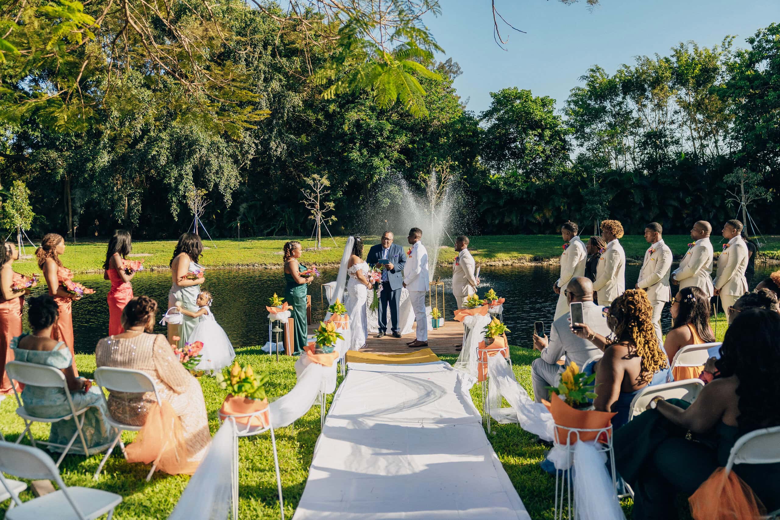 Lakeside wedding ceremony with guests and floral aisle at Saint Patrick Palace private estate in South Florida