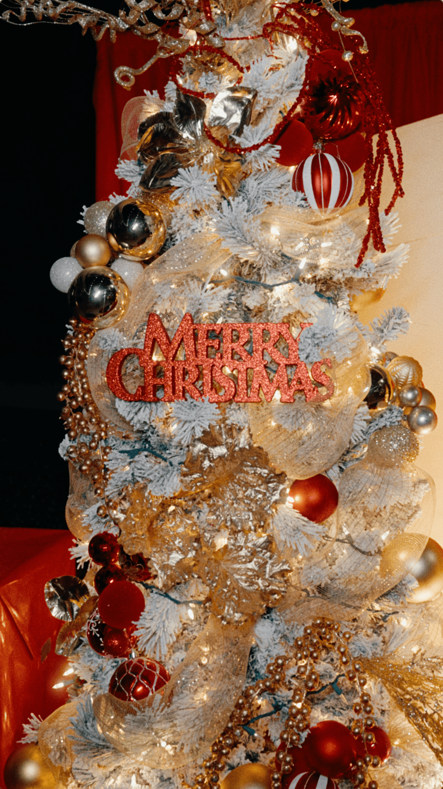 White Christmas tree with red and gold ornaments, glittering ribbons, and a Merry Christmas decoration.