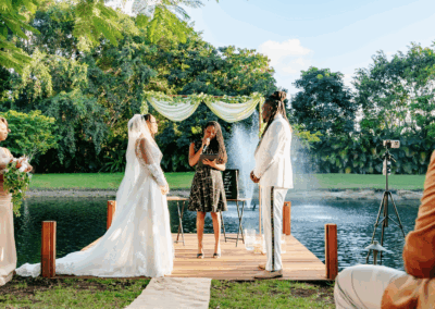 Bride and groom exchange vows on a lakeside dock with greenery and fountain backdrop at a private estate wedding.
