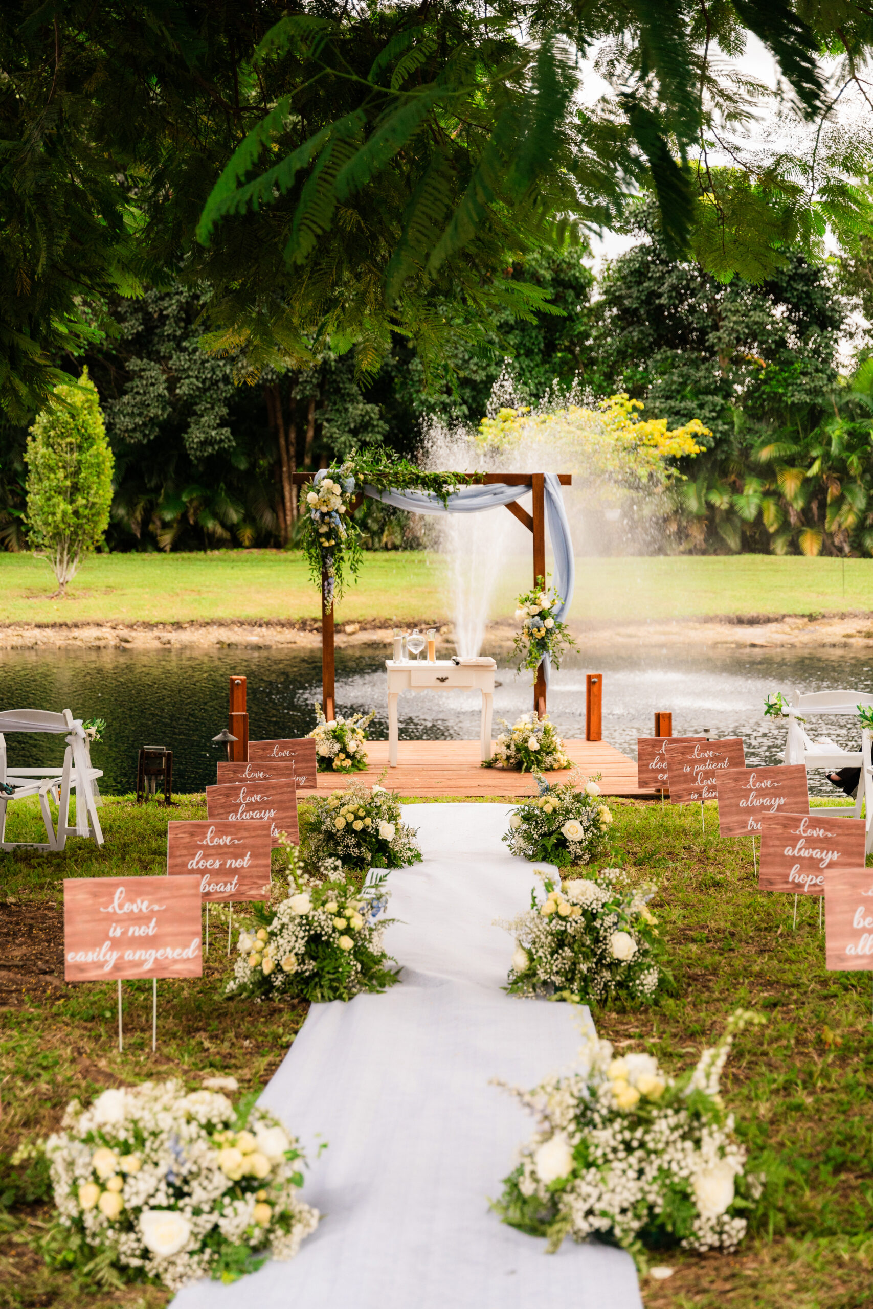 Romantic Lakeside Wedding Ceremony Setup | Outdoor Wedding Décor Inspiration Romantic lakeside wedding ceremony with floral aisle décor, rustic wooden signs, and fountain backdrop.