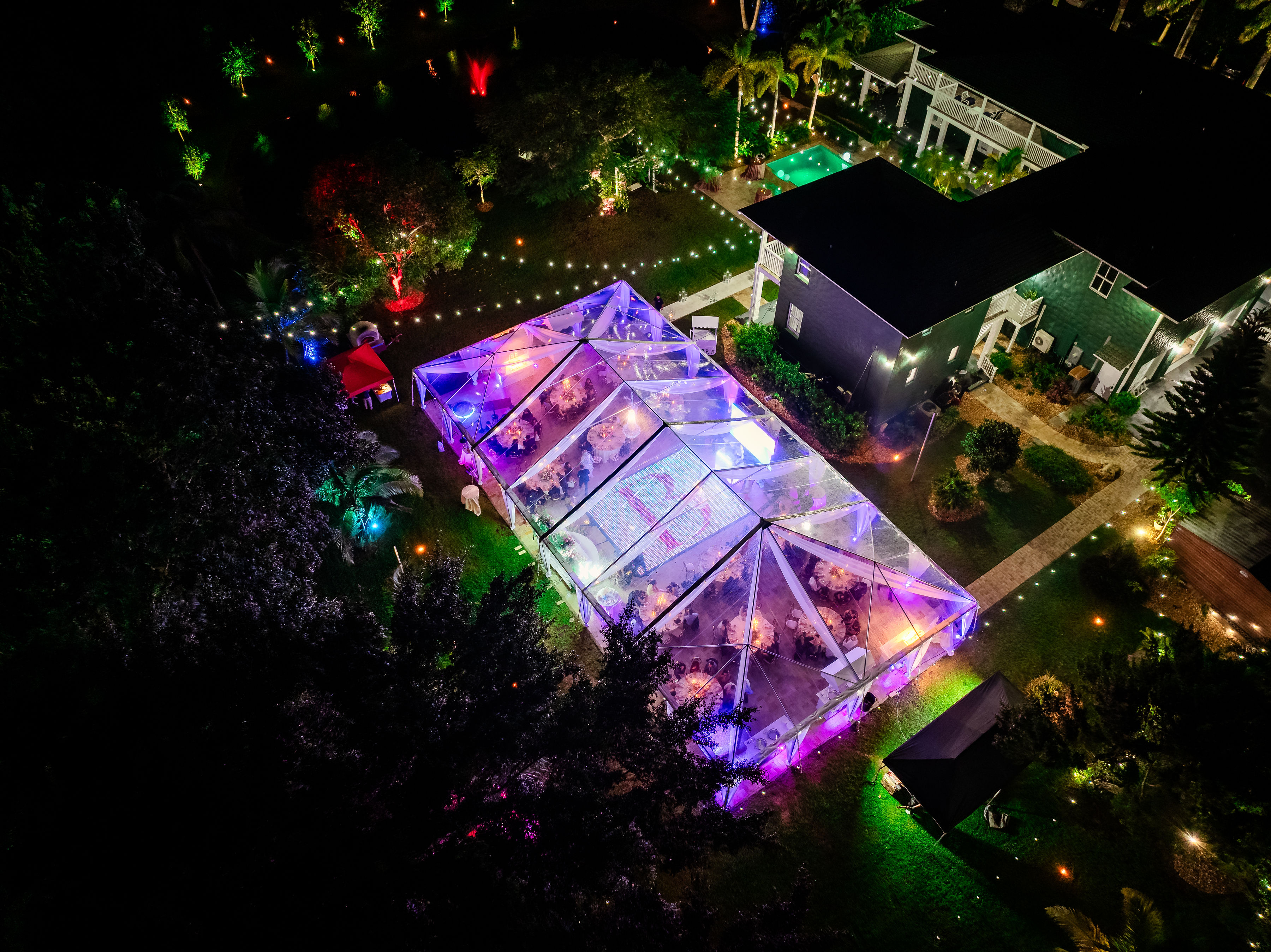 Night aerial of a rose gold quinceañera under a clear-top tent with purple lighting at Saint Patrick Palace estate.