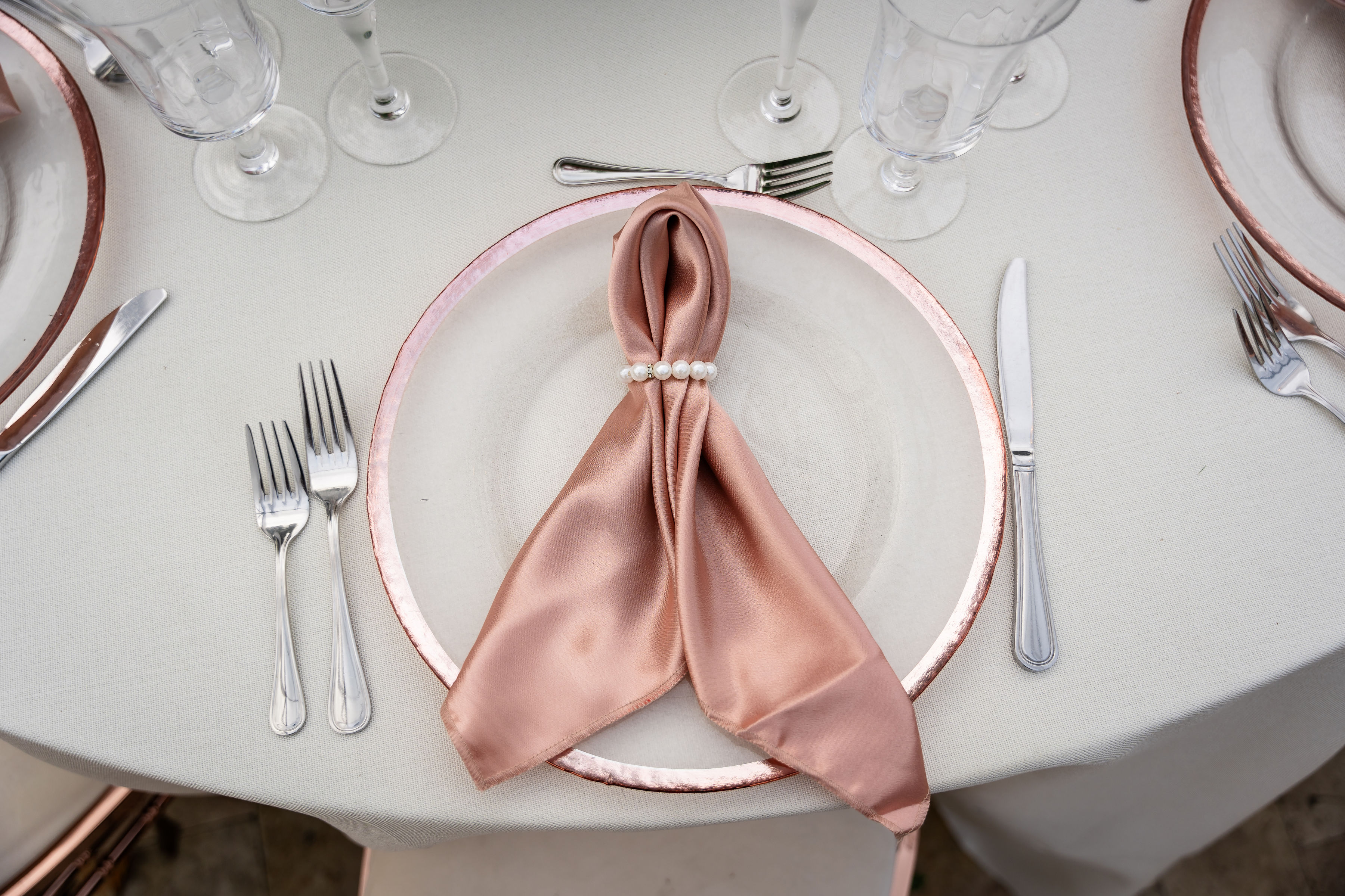 Rose gold quinceañera place setting with satin napkin, pearl ring, and elegant charger plate.