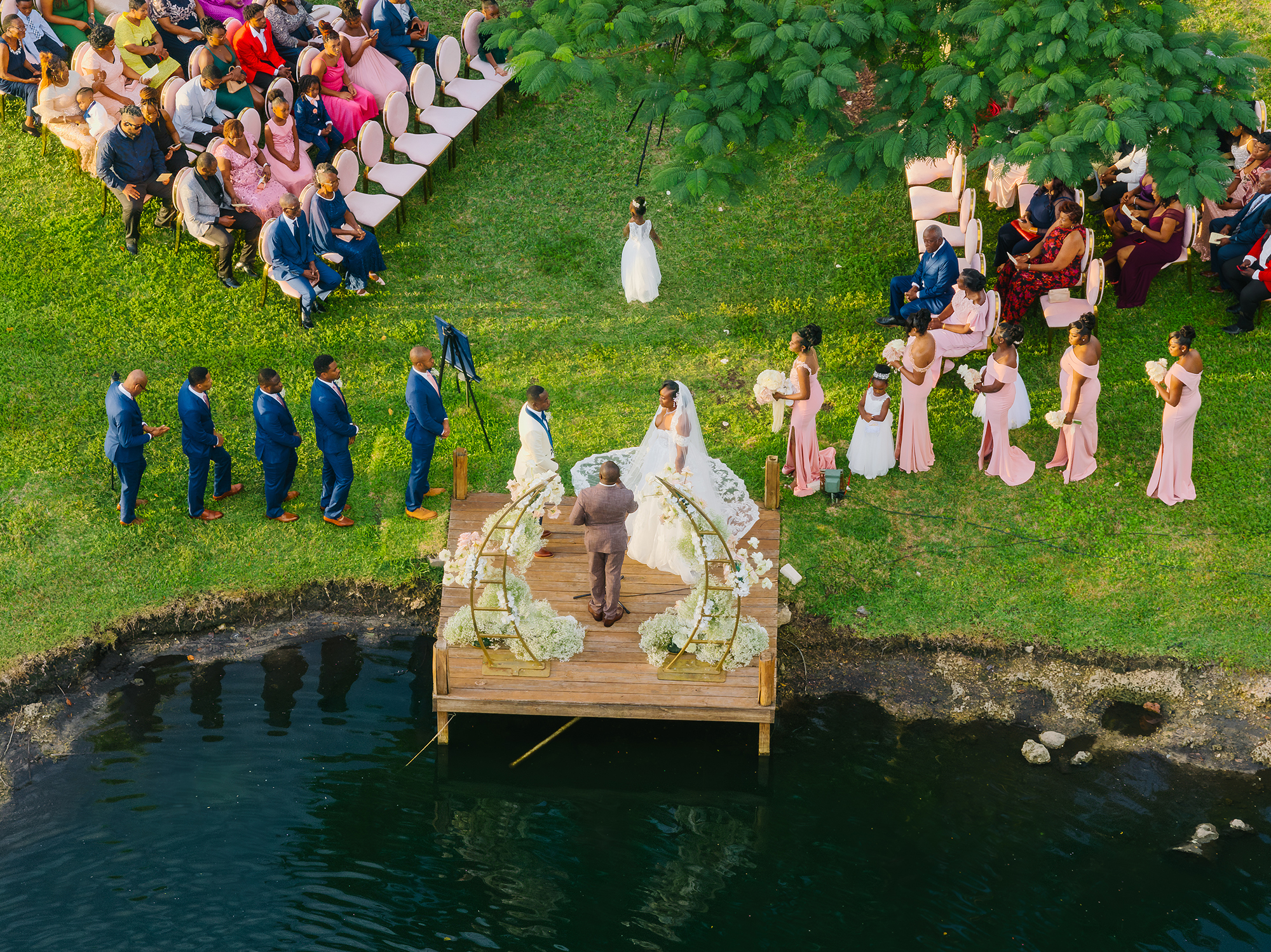 Aerial view of the lakeside dock ceremony with blush seating and wedding party at Saint Patrick Palace.