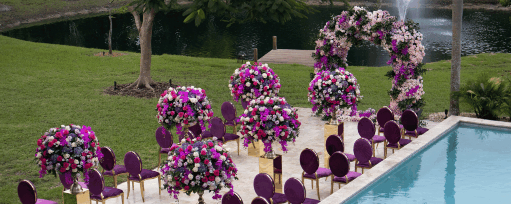 Vibrant purple and pink luxury floral wedding ceremony setup next to the lake at Saint Patrick Palace in Davie, FL.