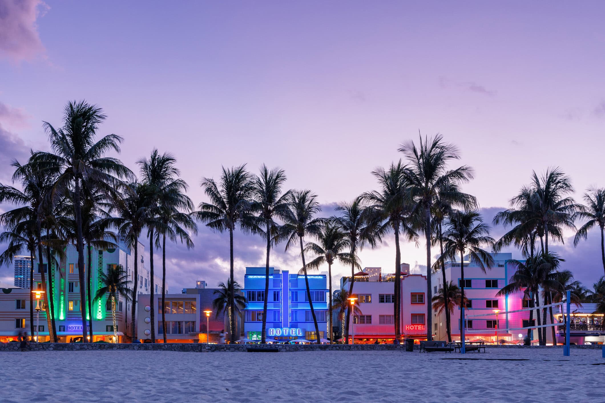 South Beach beachfront with palm trees and colorful Art Deco hotels illuminated along Miami Beach at dusk.